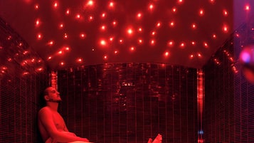 Una persona sentada en una habitación iluminada con luz roja, con pared y techo en patrón de cuadrícula.