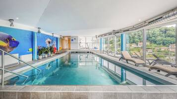 Una piscina interior con agua cristalina azul, rodeada de sillones de descanso y plantas en macetas.