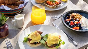Una mesa con alimentos para el desayuno, como huevos, bollería y fruta.