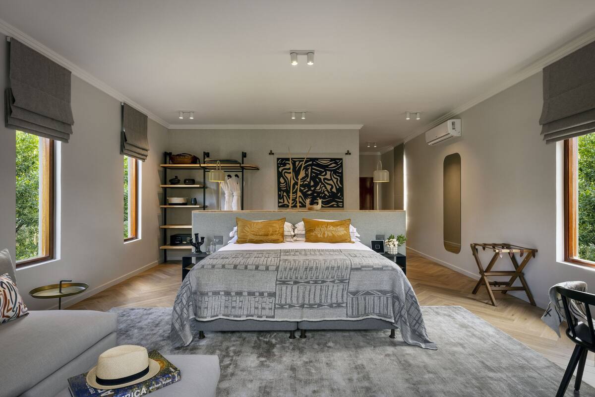 A modern bedroom with a large bed, built-in shelves, a desk, and a view of greenery.