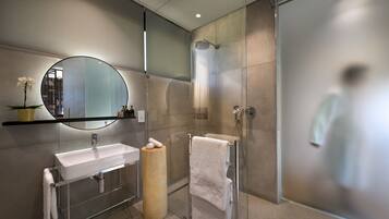 Un baño moderno con cabina de ducha de vidrio, un espejo redondo y un taburete de madera.
