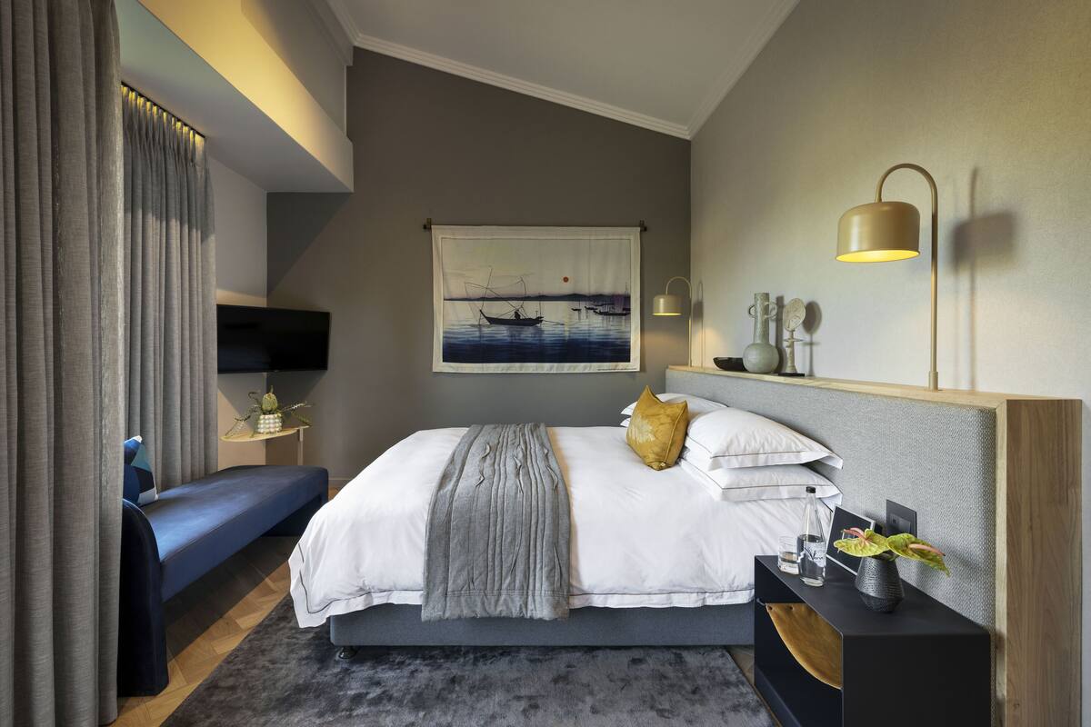 A modern bedroom with a bed, bedside table, lamp, and a painting on the wall.