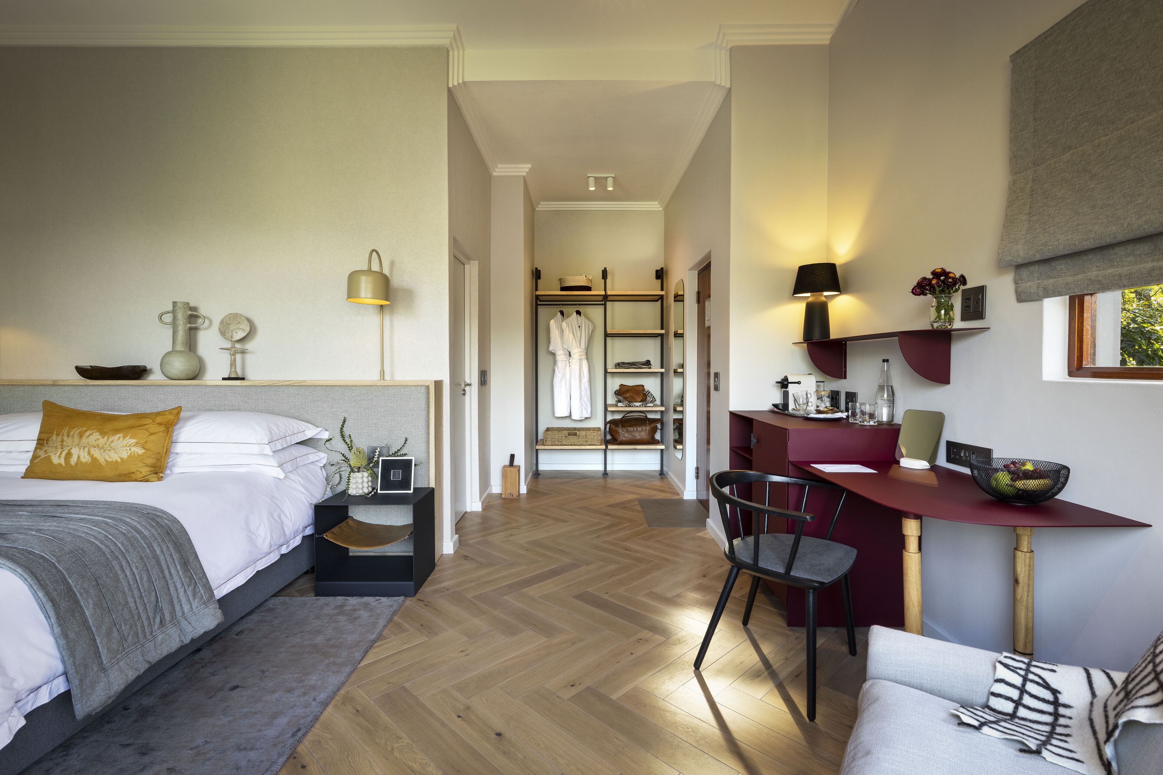 A modern bedroom with a large bed, bedside tables, a desk with a chair, and a view into a walk-in closet.