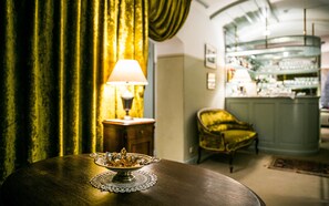 A room with a round wooden table, a decorative bowl, a lamp, a green chair, and a bar area in the background. -  Antonius Boutique Hotel (Tartu)