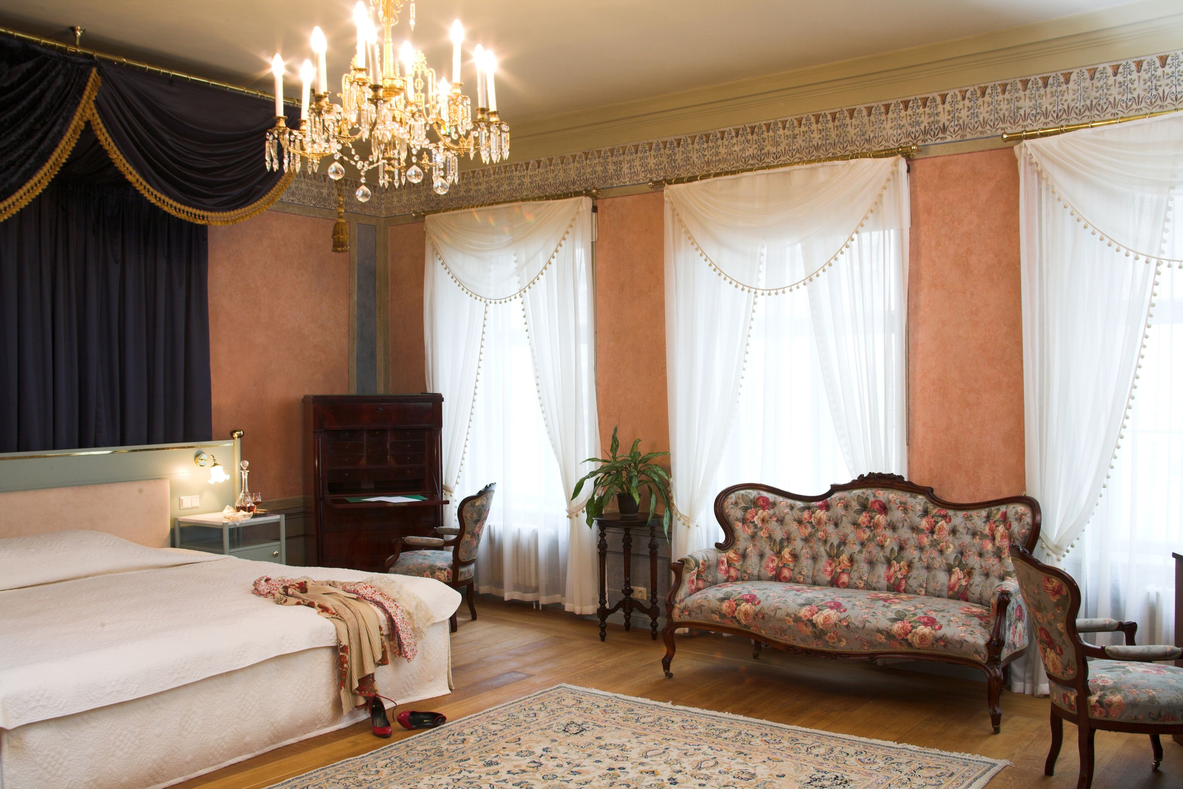 A bedroom with a large bed, a floral sofa, a wooden cabinet, and a chandelier.