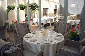 A round dining table set for six with wicker chairs, white tablecloths, and hanging flower baskets. -  Antonius Boutique Hotel (Tartu)