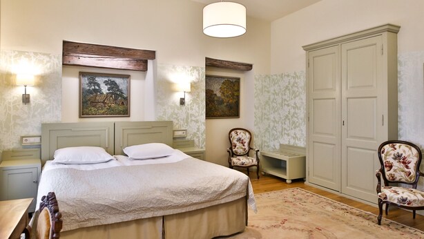 A bedroom with a bed, two nightstands, a chair, a wardrobe, and two wall-mounted lamps. -  Antonius Boutique Hotel (Tartu)