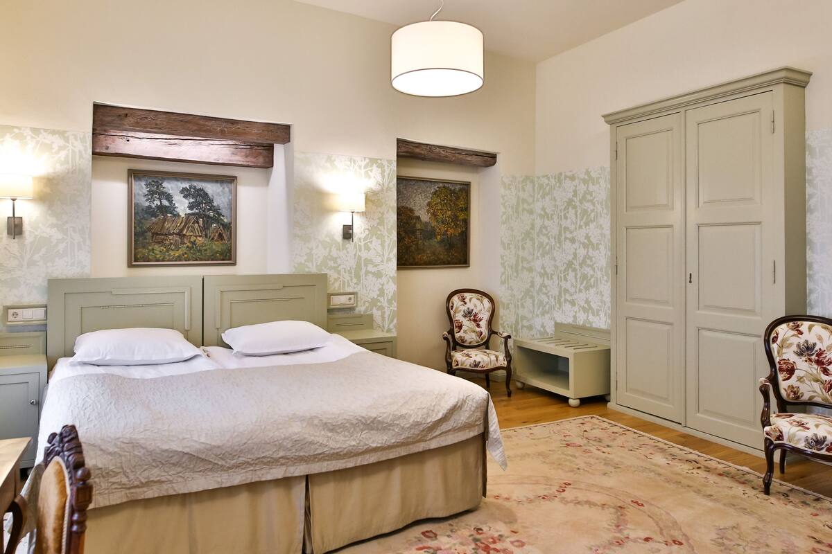 A bedroom with a bed, two nightstands, a chair, a wardrobe, and two wall-mounted lamps.