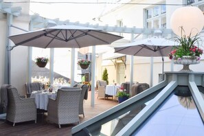 An outdoor dining area with wicker chairs and tables, umbrellas, and hanging flower baskets. -  Antonius Boutique Hotel (Tartu)