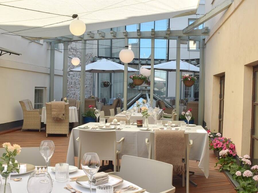 An outdoor dining area with tables set for two, surrounded by wicker chairs and covered by umbrellas.