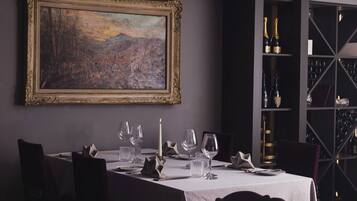 Een eetkamer met een tafel gedekt voor vier personen, een lijst met een schilderij aan de muur en een wijnrek op de achtergrond.
