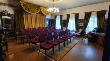 Um quarto com fileiras de cadeiras vermelhas, uma escrivaninha de madeira e um espelho à esquerda.