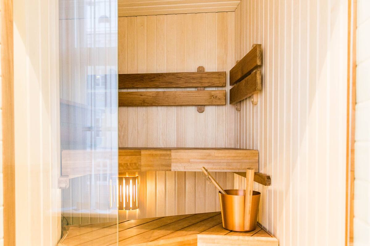 A sauna with wooden benches, a wooden floor, and a copper bucket with a wooden spoon.