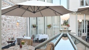 An outdoor dining area with tables, wicker chairs, and umbrellas. There are hanging flower baskets and a glass balustrade. -  Antonius Boutique Hotel (Tartu)