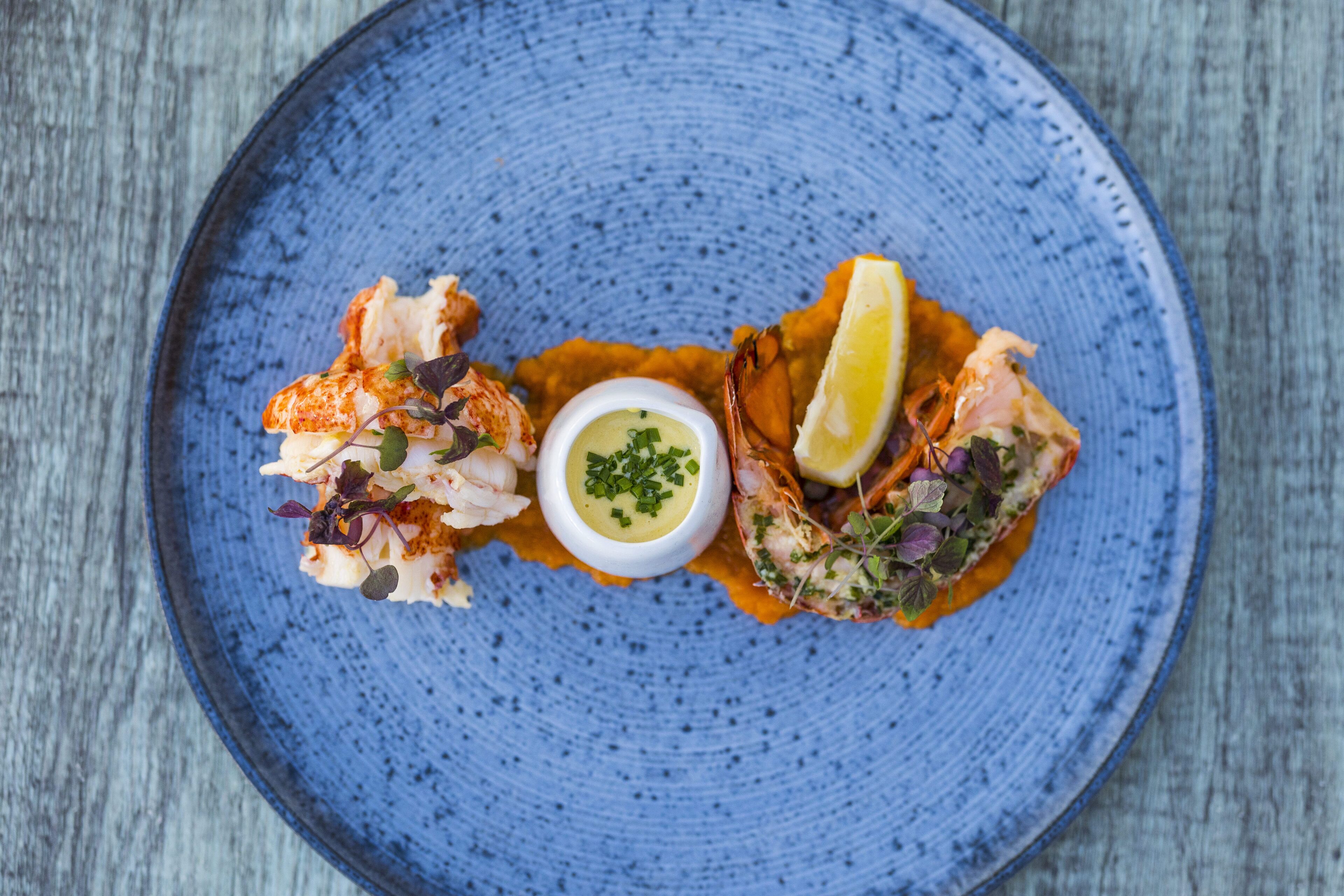 Un plato azul de cerámica con mariscos, un gajo de limón y un recipiente pequeño con salsa.