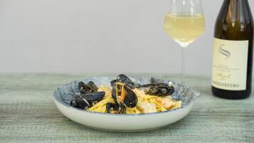 Un plato de mejillones con pasta, una copa de vino blanco y una botella de vino sobre una mesa de madera.