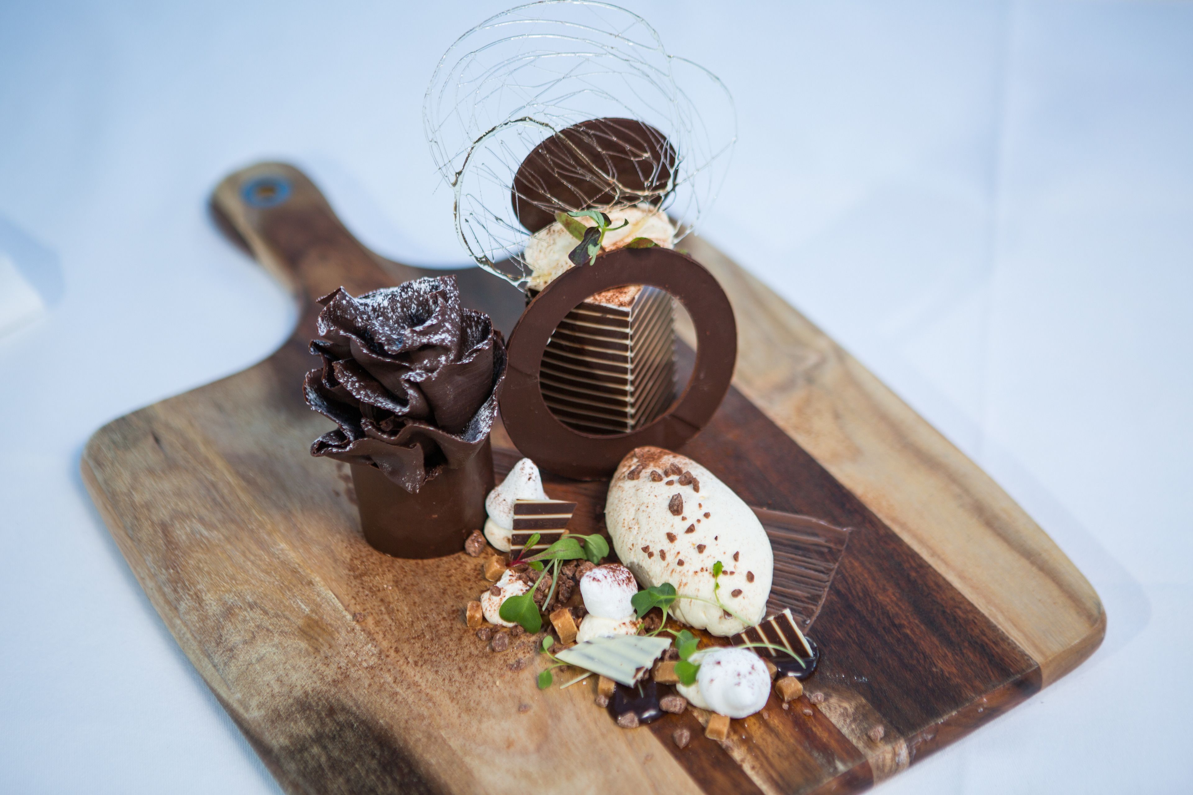 Een houten plank met diverse chocolade- en dessertproducten, waaronder een chocoladesculptuur en een chocoladebol.