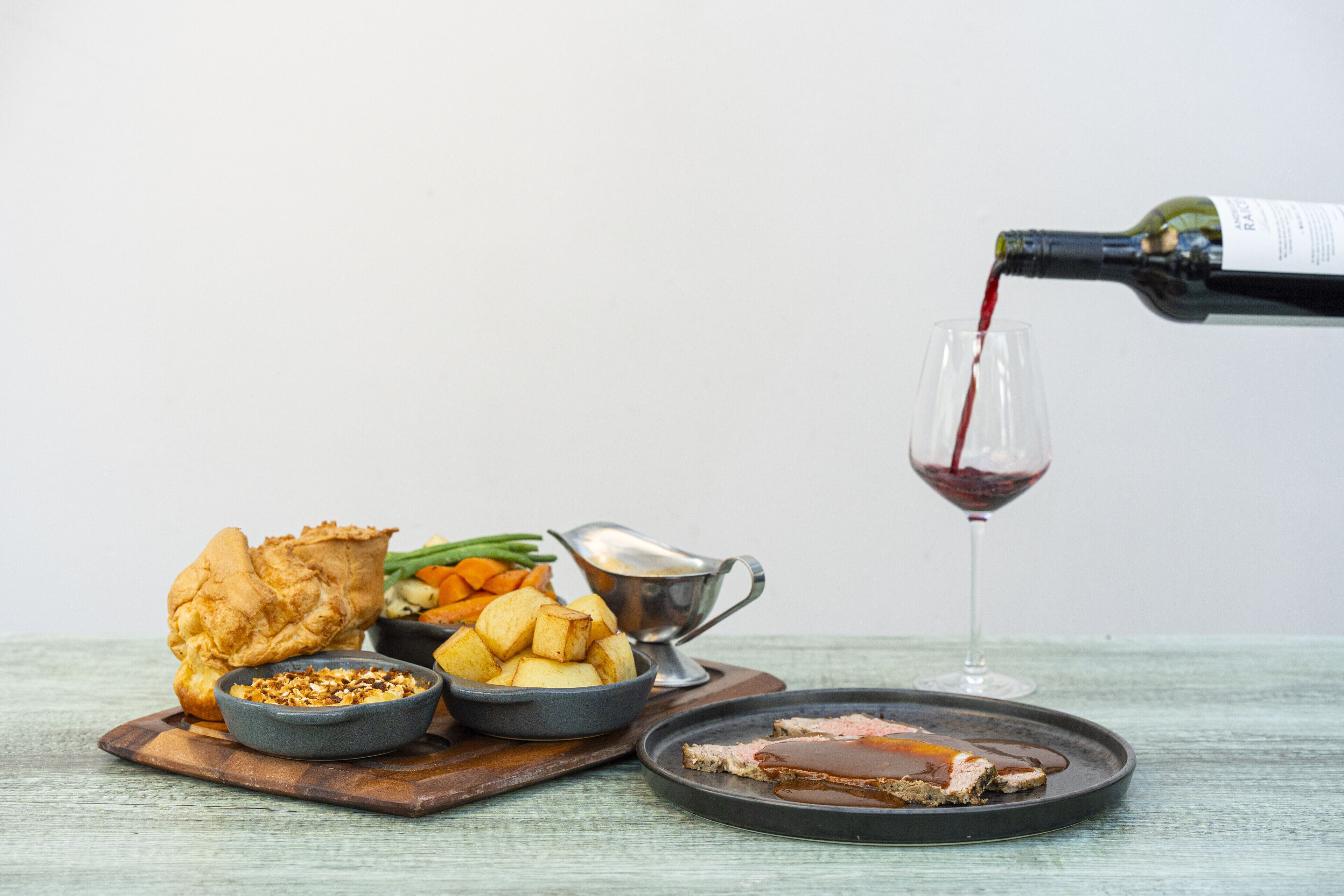 Un plato con carne asada, papas y una jarra para salsa, mientras se sirve vino en una copa.