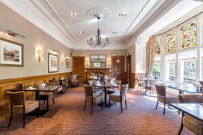 A spacious dining area with multiple tables and chairs, a chandelier, and large windows with stained glass. - Sherbrooke Castle Hotel (Glasgow)