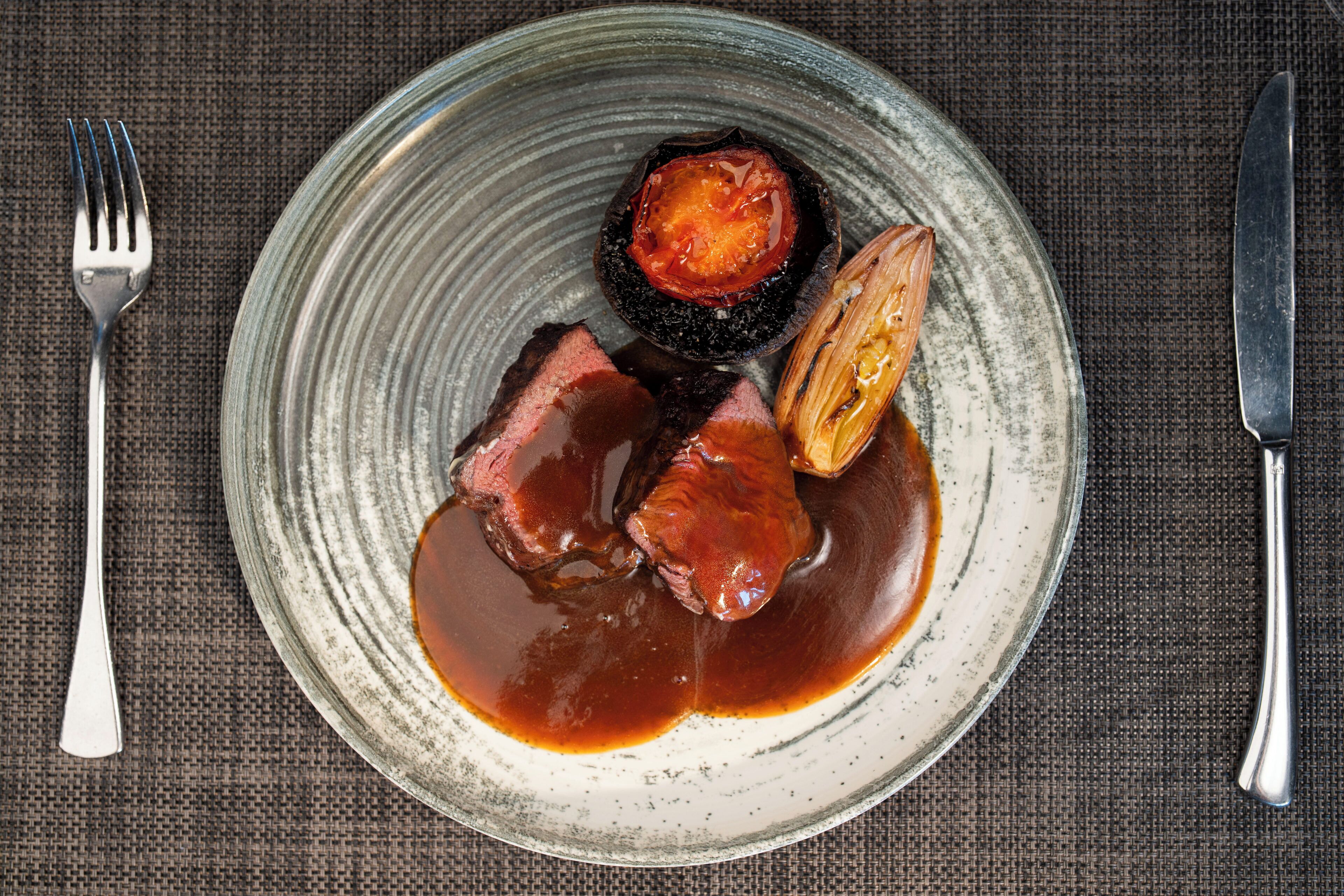 A plate with a dark, glazed fruit, a slice of meat, and a sauce.