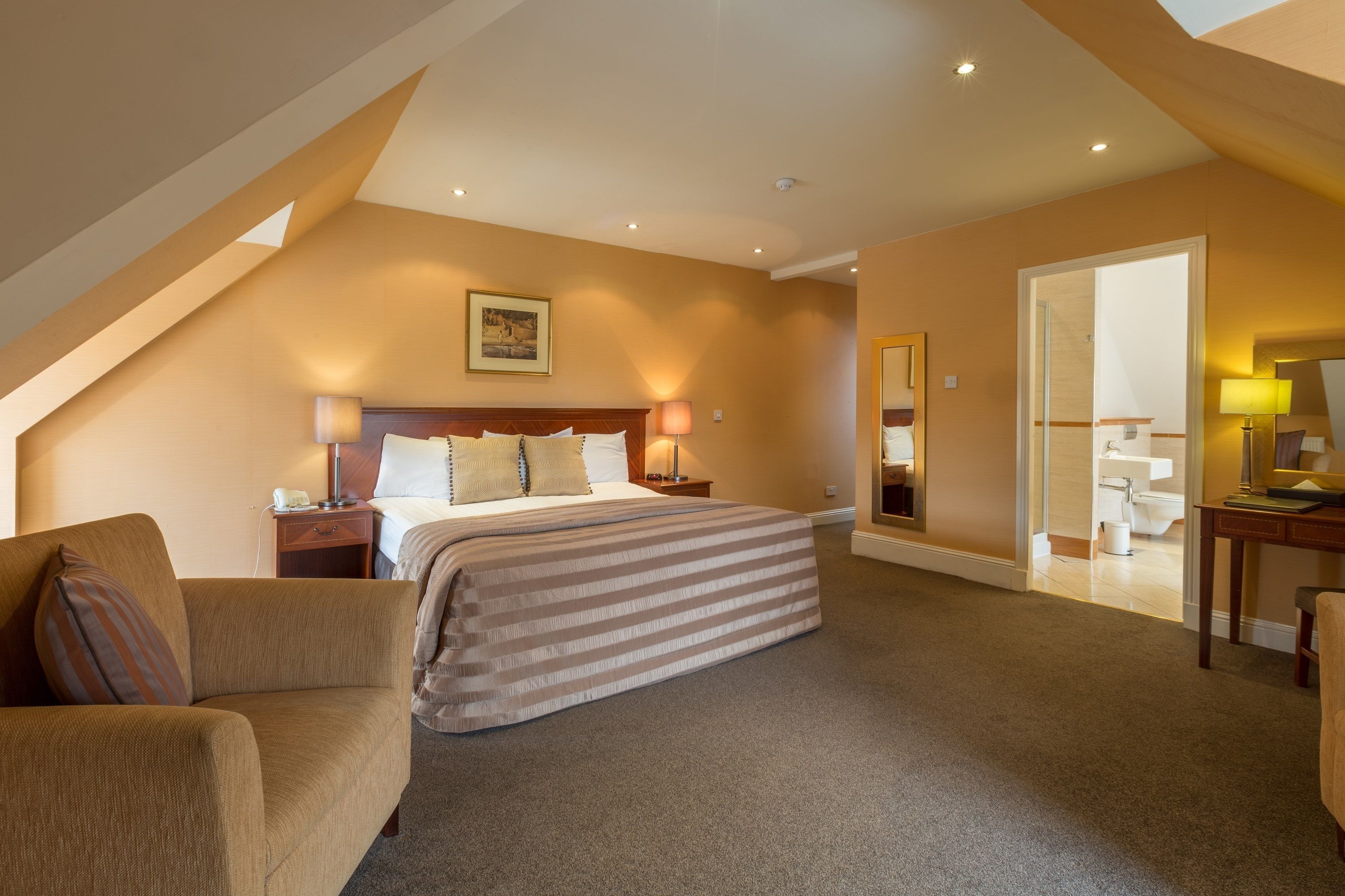 A hotel room with a large bed, a sofa, a desk, and a bathroom visible through an open door.