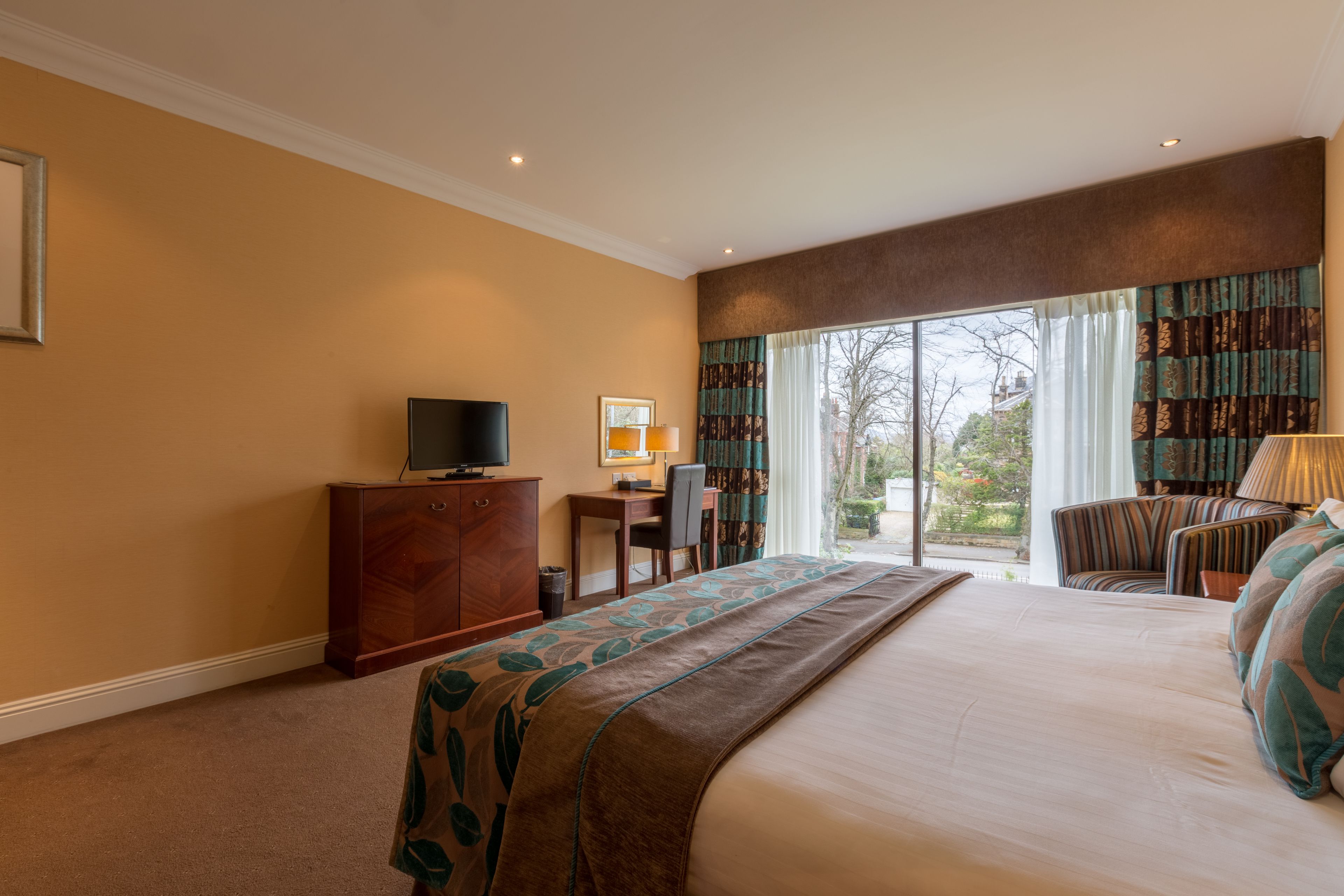Habitación de hotel con una cama grande, un escritorio, un televisor y vistas al exterior a través de amplias ventanas.