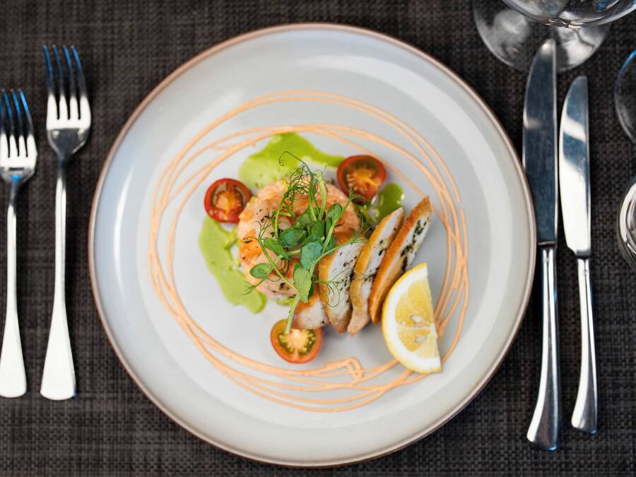 A plate of food with a salad, shrimp, and lemon on a white plate with orange lines.