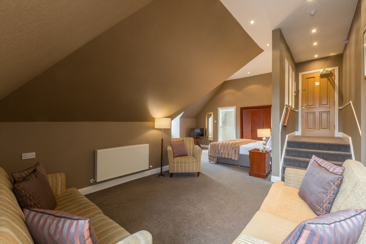 A spacious room with a high ceiling, a cozy seating area, a bed, a television, and a staircase leading to an upper level.
