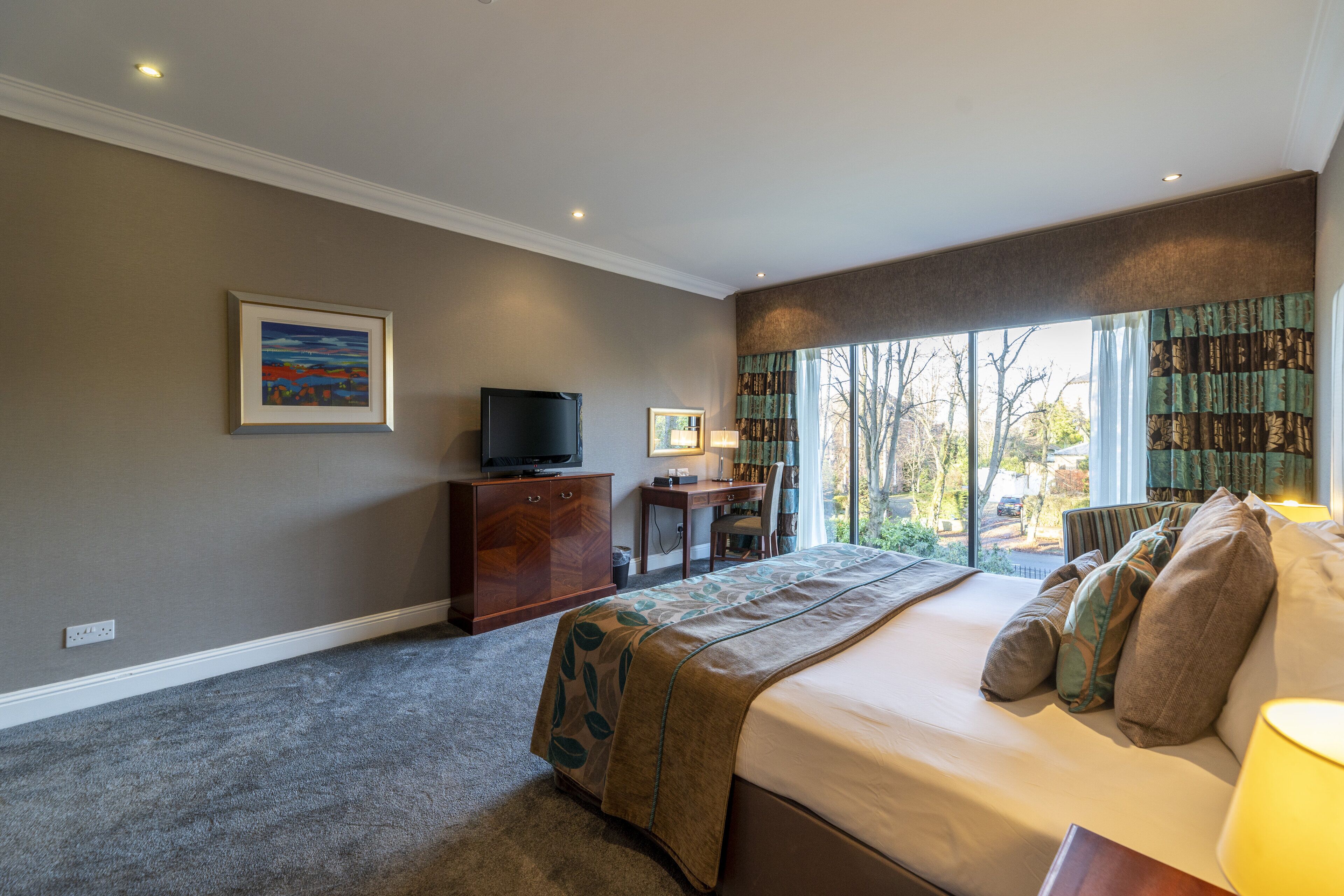 A hotel room with a large bed, a desk with a chair, a television, and a window with curtains.