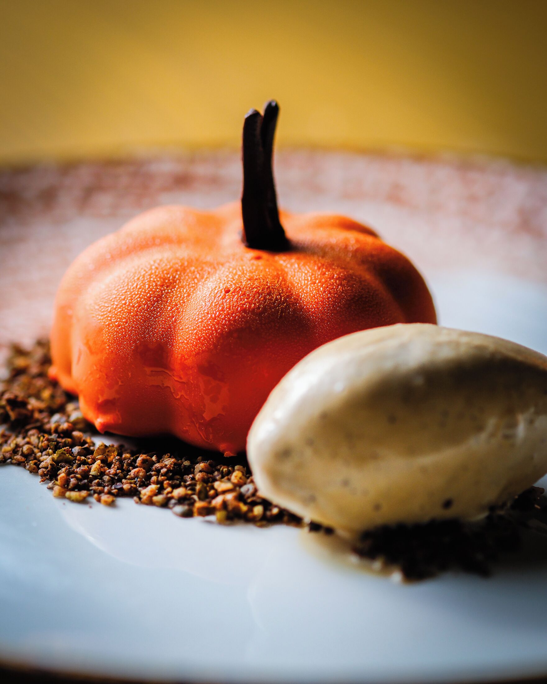 A dessert with a pumpkin and a scoop of ice cream on a plate with scattered seeds.