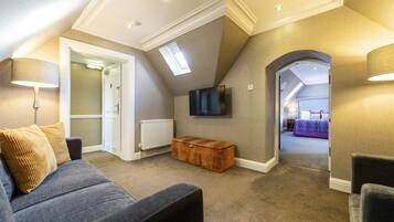 A cozy loft bedroom with a sloped ceiling, a large window, a flat-screen TV, and a view into another room.