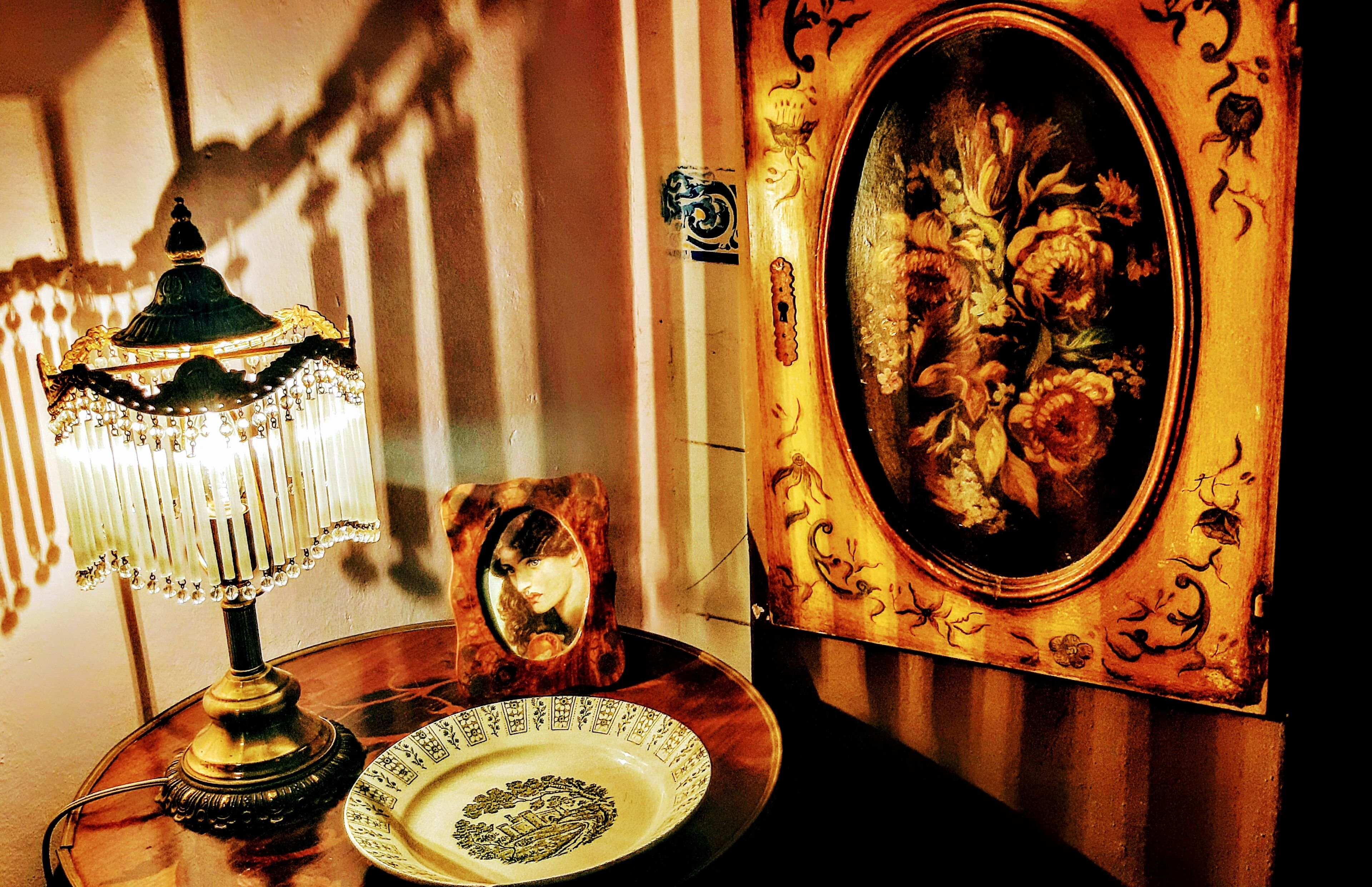 A table with a table lamp, a framed mirror, and a plate with a floral design.