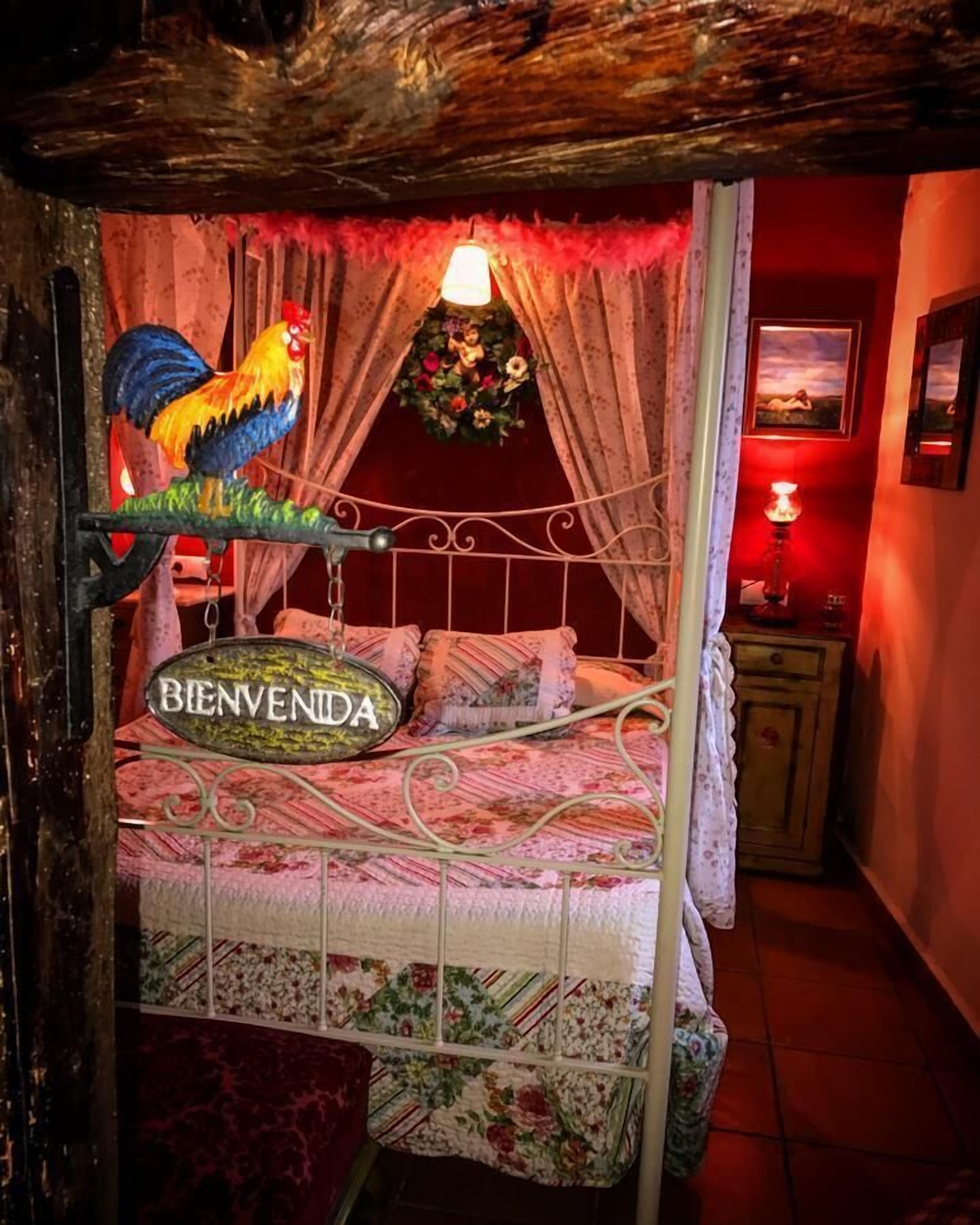 Un lit avec une pancarte indiquant « BIENVENIDA », une décoration représentant un coq et une couvre-lit à motifs floraux.