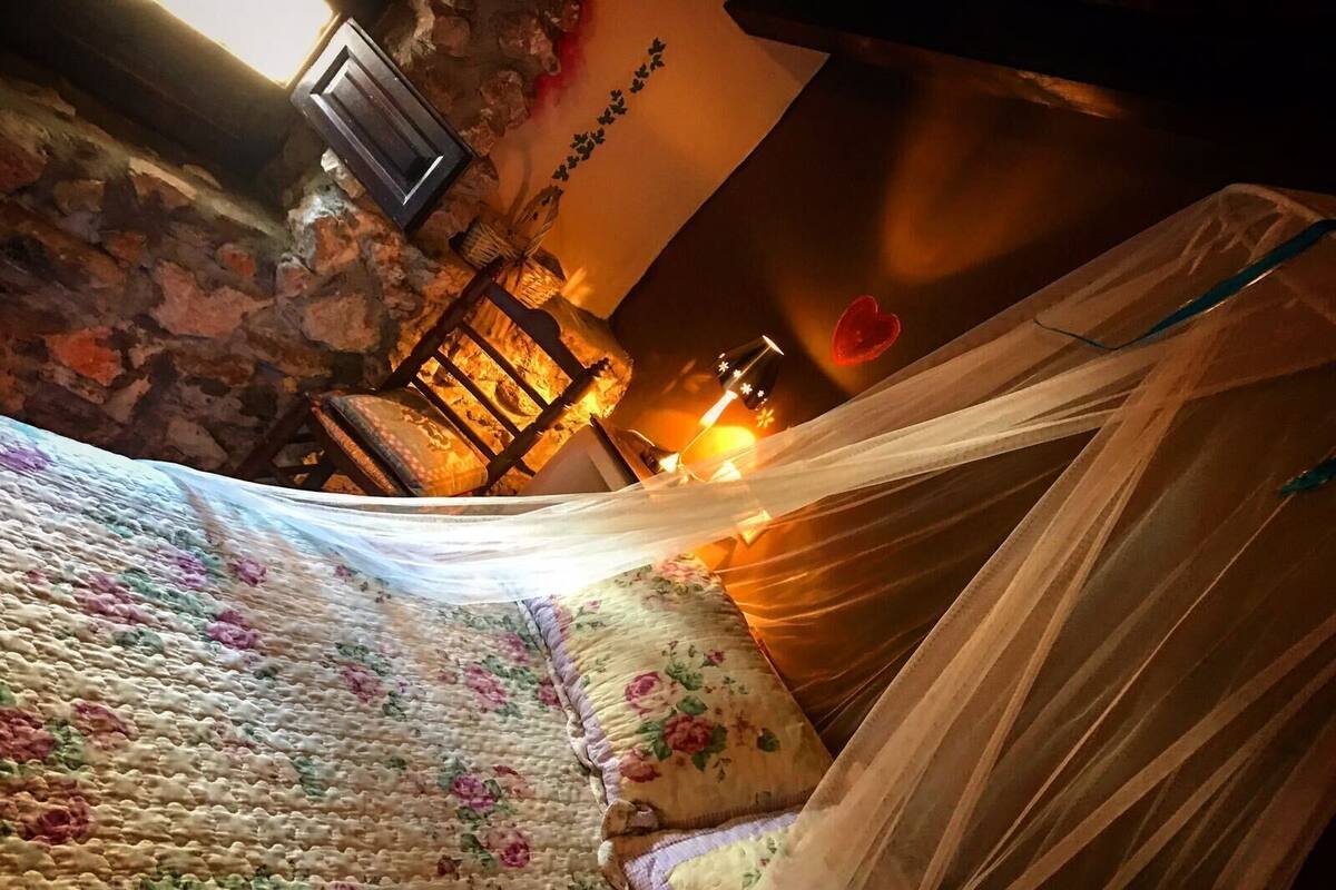 A bed with a floral-patterned bedspread, a wooden headboard, and a stone wall in the background.