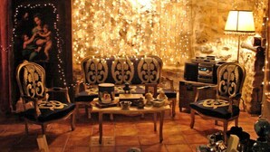 Une pièce chaleureuse avec un mur en pierre, un canapé, deux fauteuils, une table sur laquelle se trouvent divers objets et une lampe.