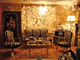 Una habitación acogedora con pared de piedra, un sofá, dos sillones, una mesa con diversos objetos y una lámpara.