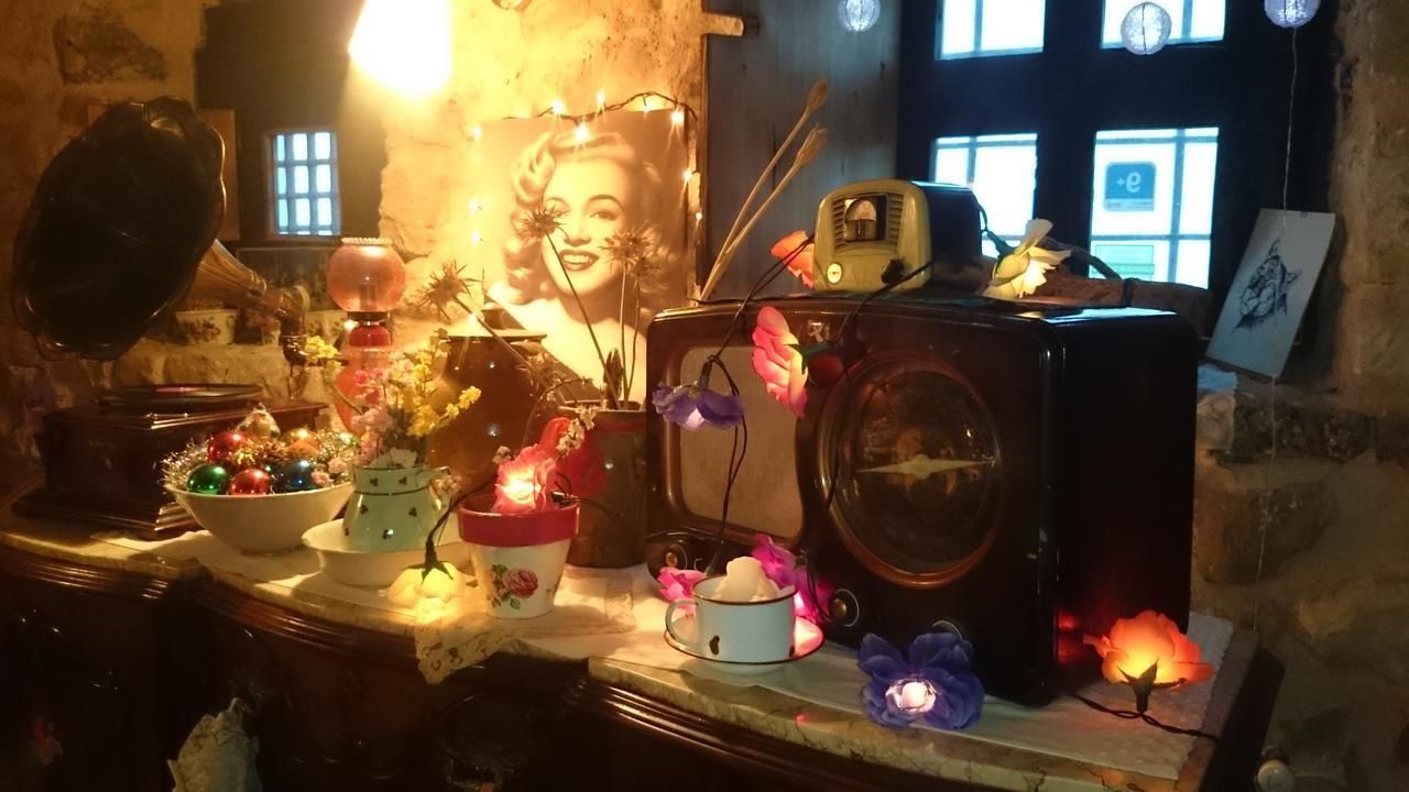 Una radio antigua, una lámpara y varios objetos decorativos sobre una mesa en una habitación con paredes de piedra y una ventana.