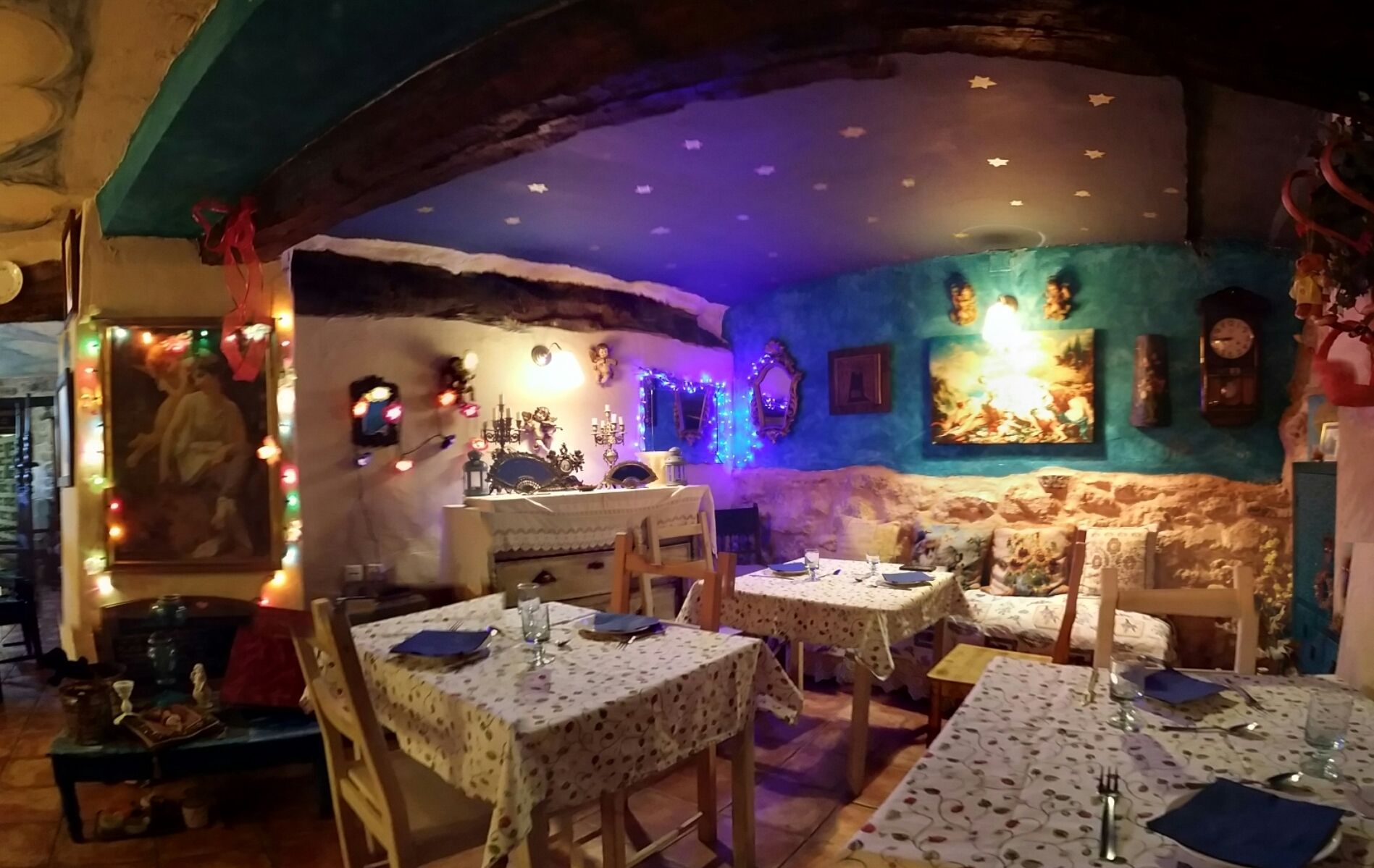 Een restaurant met meerdere tafels gedekt voor diners, een muurschildering en decoratieve verlichting.