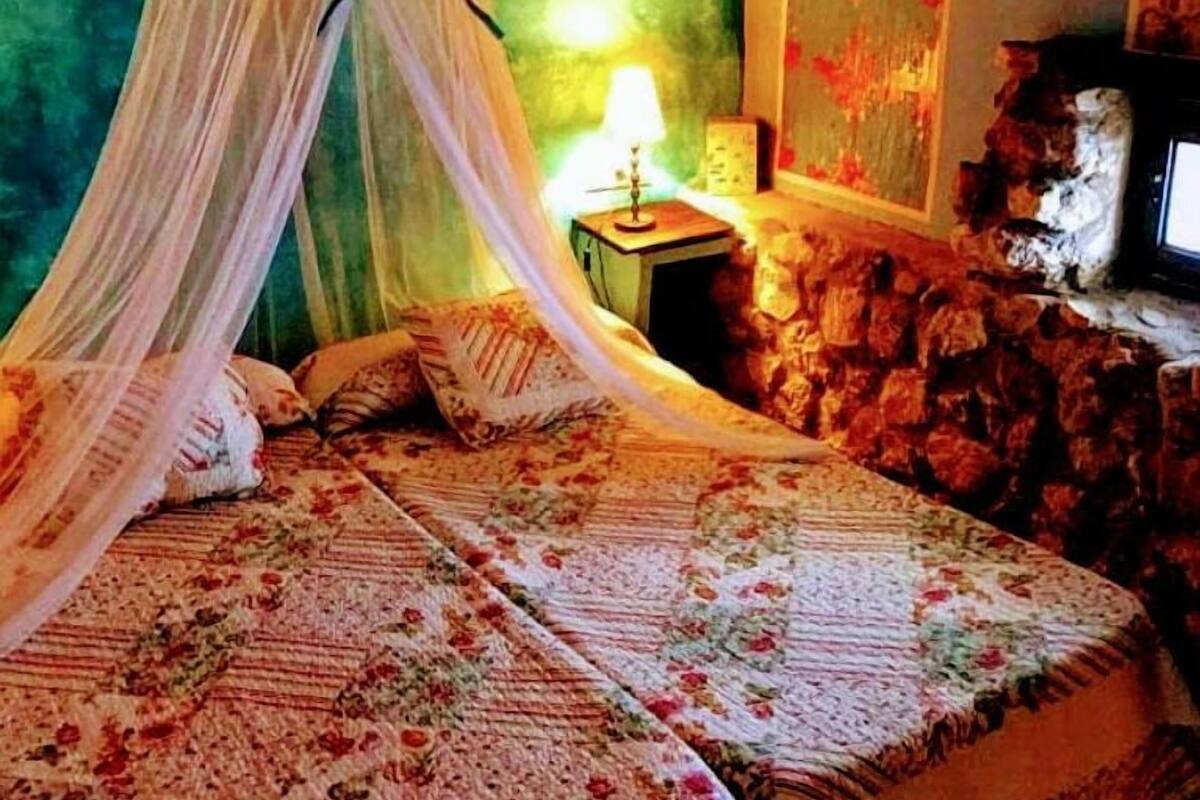 A bed with a canopy, a nightstand with a lamp, and a stone wall.
