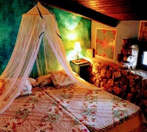Ein Bett mit Baldachin, ein Nachttisch mit Lampe und eine Steinwand.