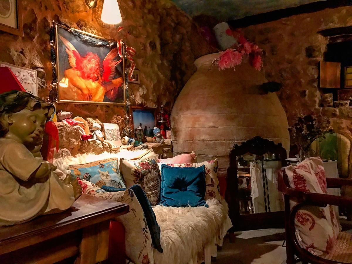 Een rustieke kamer met een stenen muur, een grote keramieken pot en diverse decoratieve objecten, waaronder een beeldje, een schilderij en een comfortabele fauteuil.
