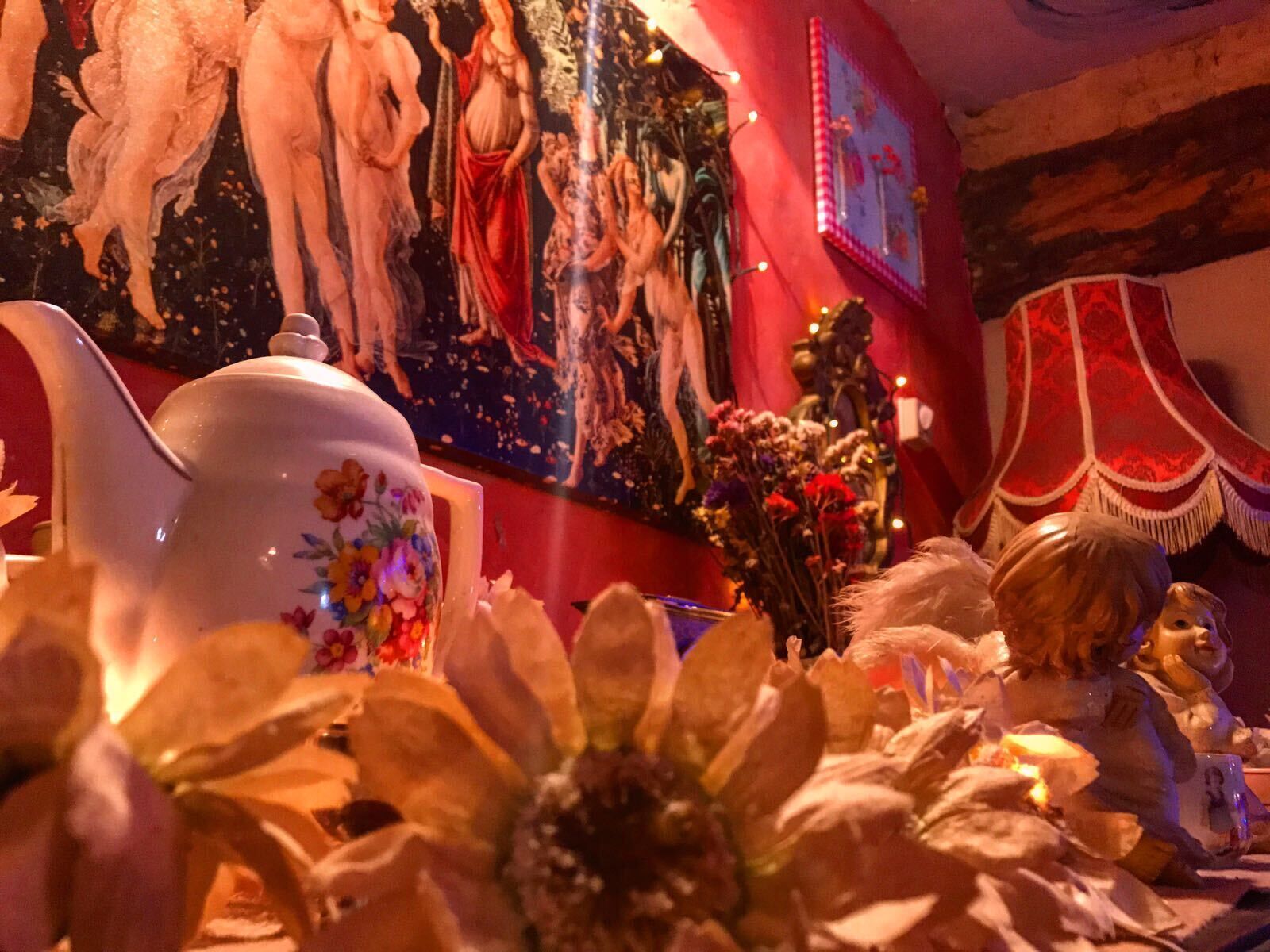 A room with a floral-patterned teapot, a painting of cherubs, and a red curtain.