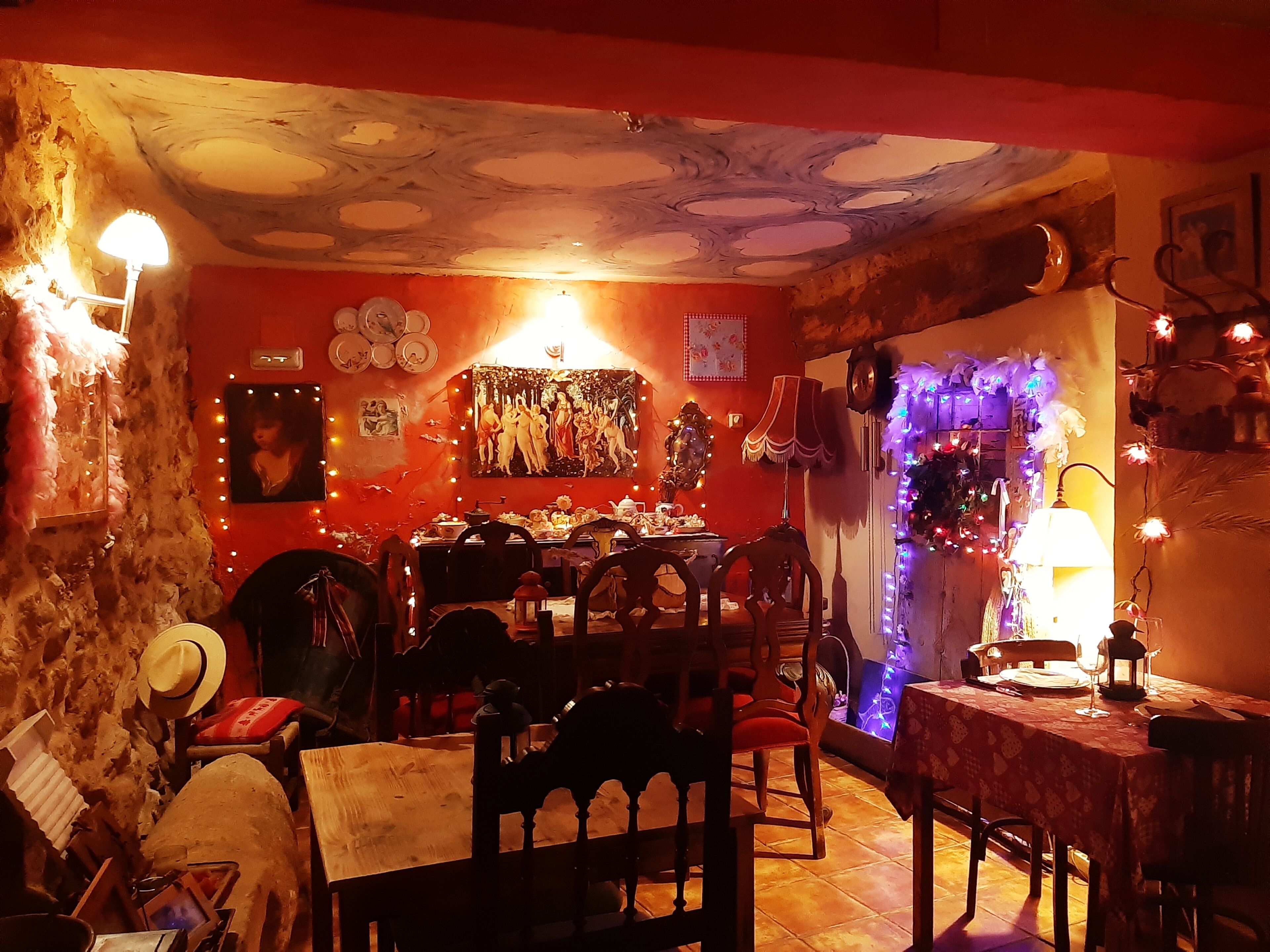 Una zona de menjador acollidora amb taula i cadires de fusta, un sostre amb disseny singular i diverses decoracions, incloent llums de llum i quadres emmarcats.