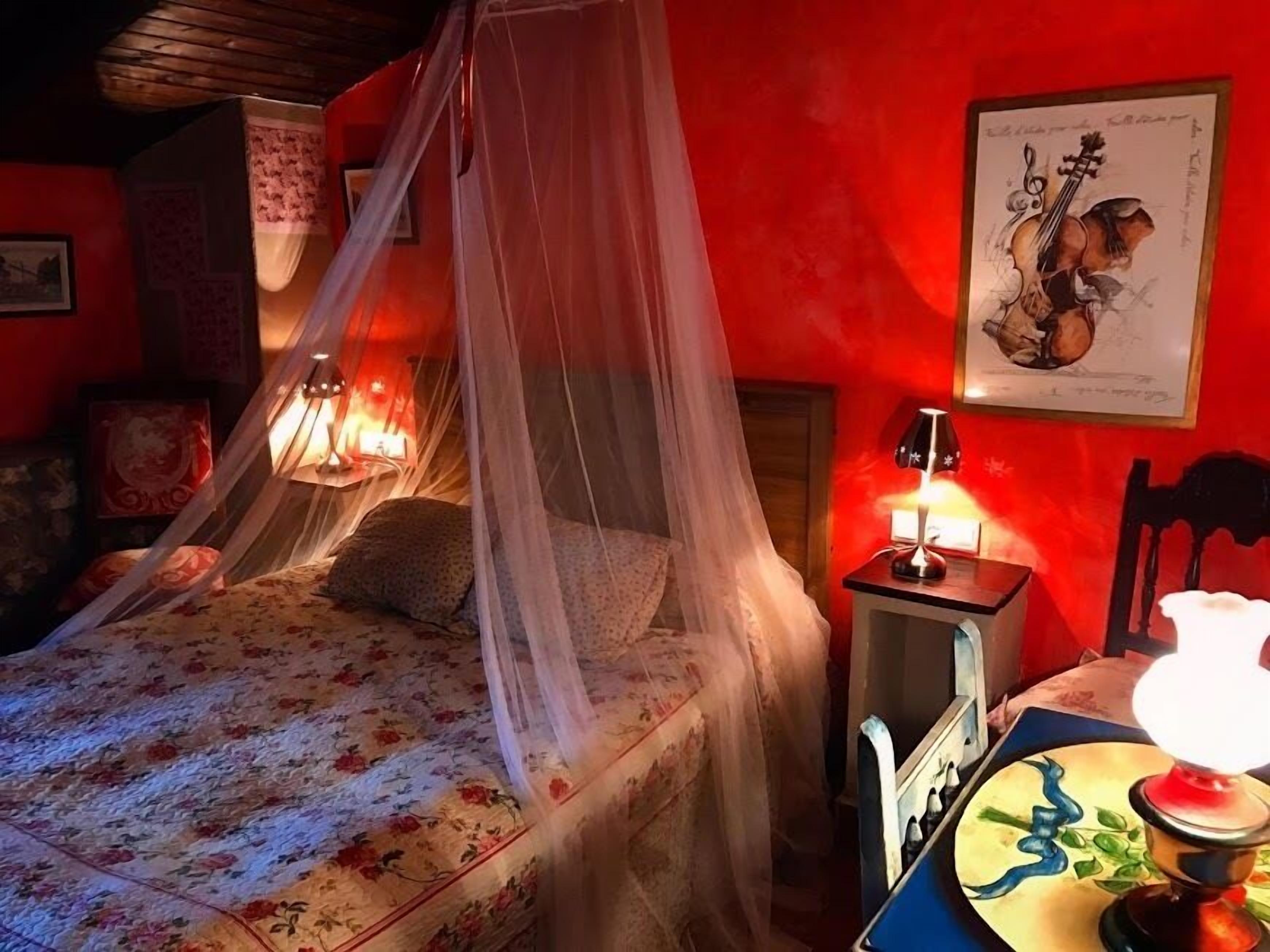 Een bed met hemel, een nachtkastje met lamp en een lijst met afbeelding aan de muur.