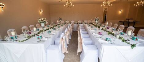 A long dining table with white tablecloths, chairs, and centerpieces.