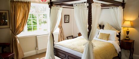 A four-poster canopy bed with a wooden frame, white bedding, and a bedside table with a lamp.