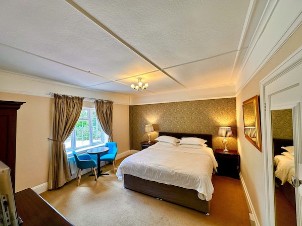 A hotel room with a large bed, a desk, and two chairs. - Claverton Country House Hotel (Battle)