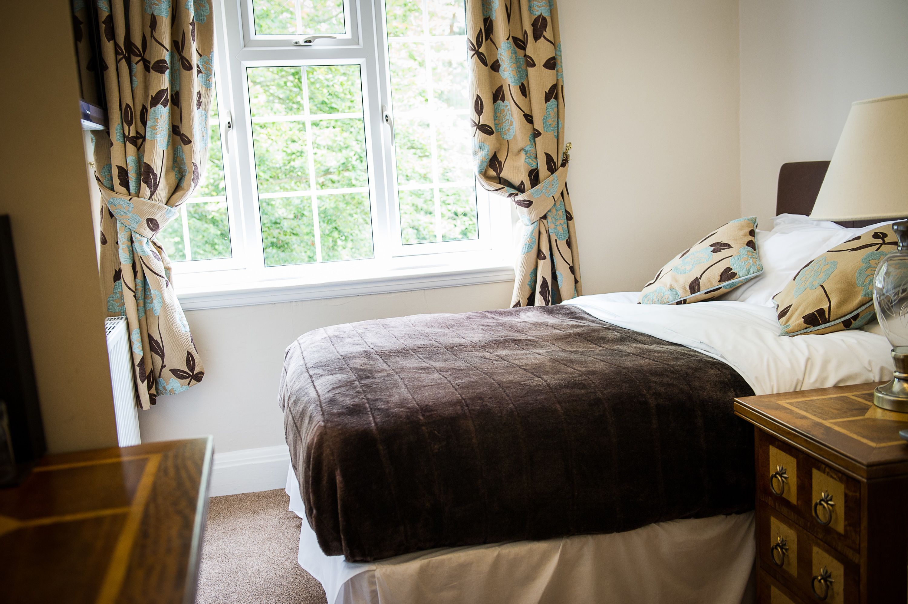 A bedroom with a bed, a nightstand, a lamp, and curtains.