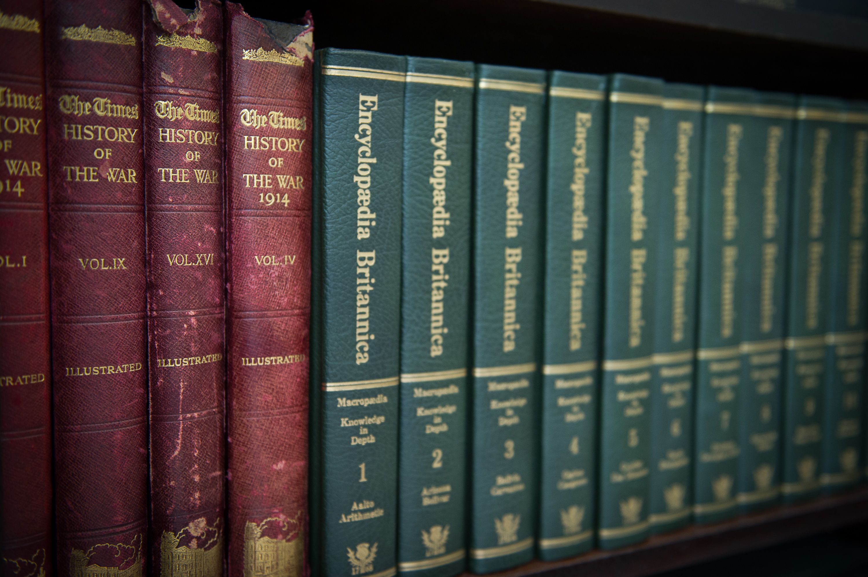 Een rij boeken op een plank, waaronder edities van 'The Times' en 'Encyclopaedia Britannica'.