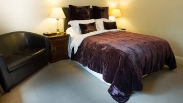 A bedroom with a large bed, two bedside lamps, a dark leather chair, and a wooden nightstand.